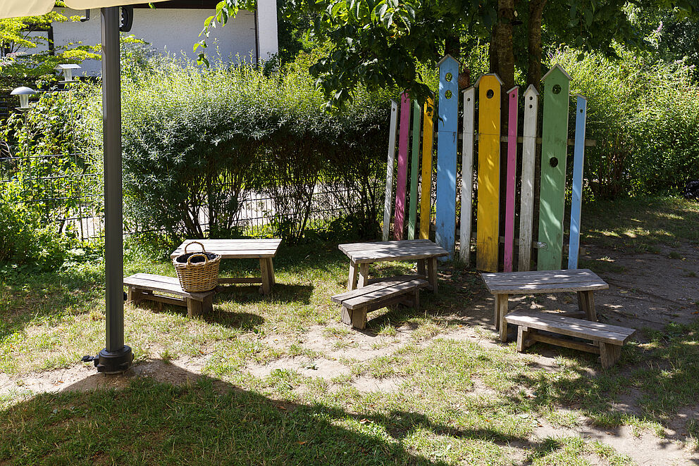 Wiese mit Kindergartenmöbelgarnituren und buntem Gartenzaunelement