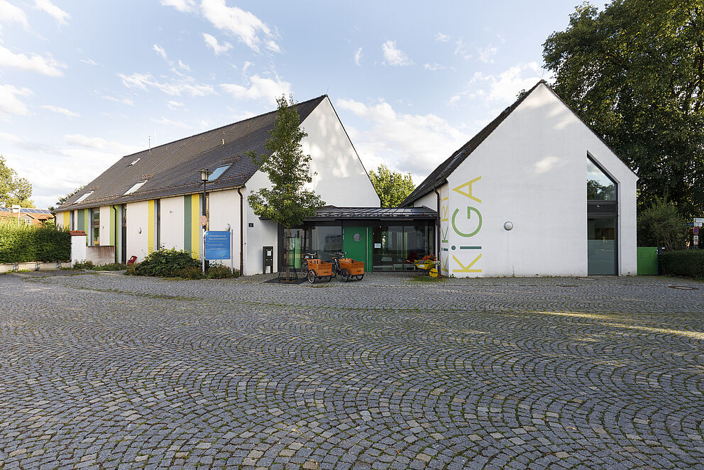 gepflasterter Platz mit zwei Gebäuden, die durch einen Glasbau miteinanderverbunden sind