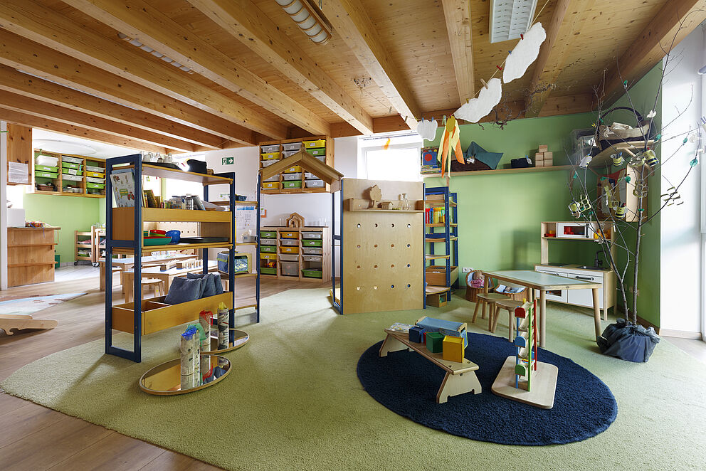 Gruppenraum mit Stellelementen, Teppichen, Kinderspielen und Regalen