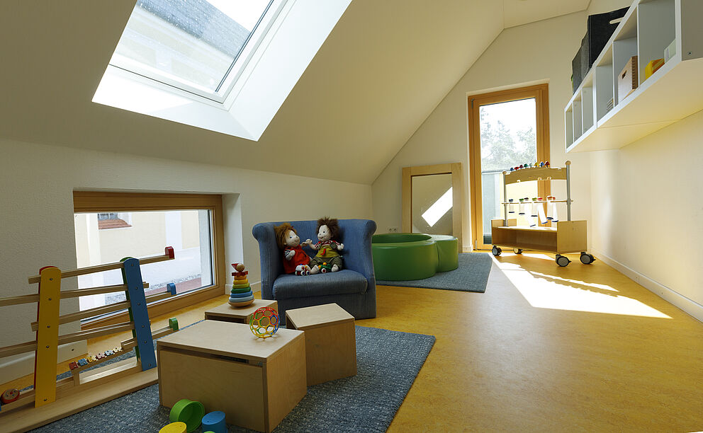 Dachgeschoßzimmer mit einem Sessel auf dem zwei Puppen sitzen, Spielsachen im Vordergrund